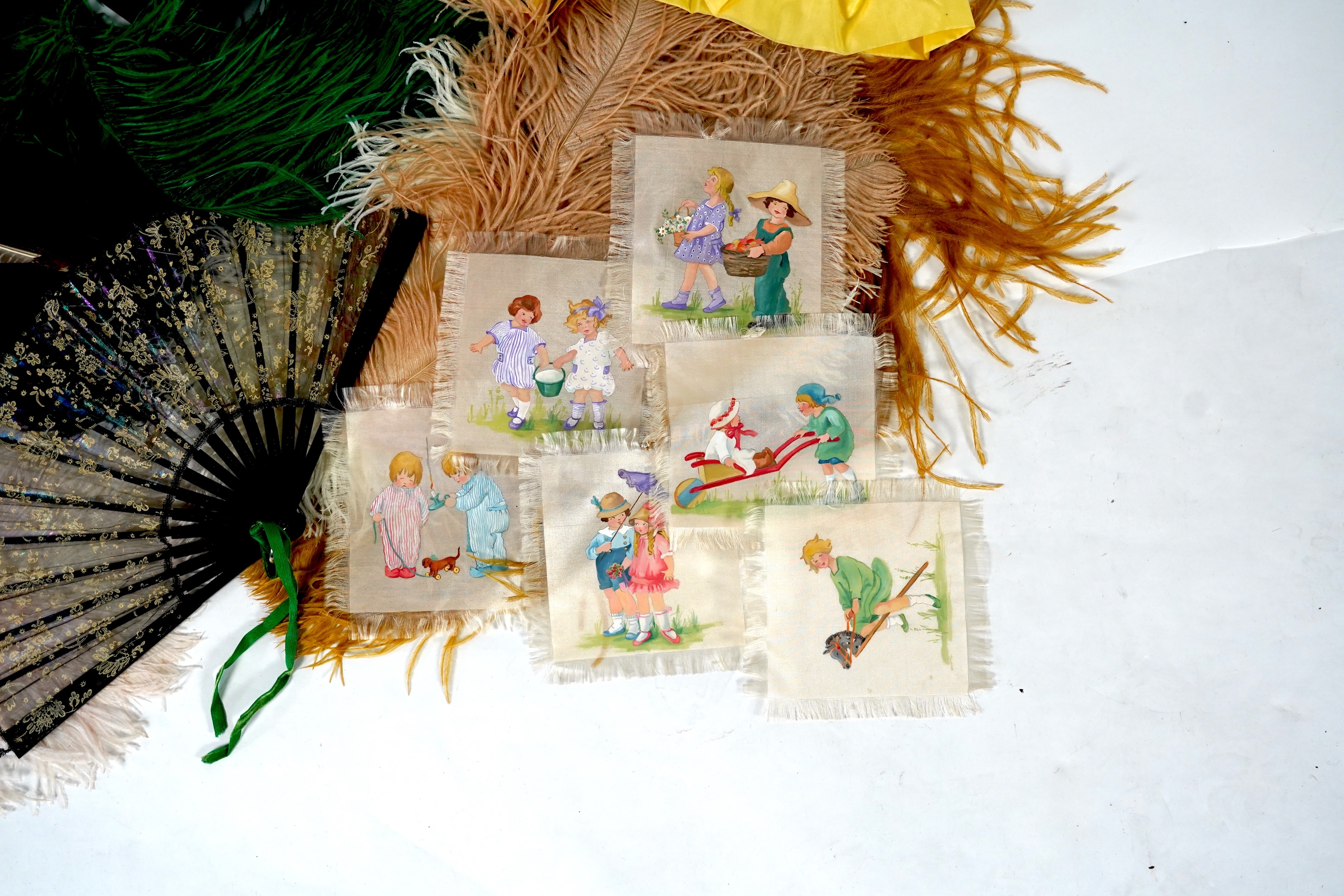 A collection of Edwardian exotic feather hat ornaments, with a collection of coloured ostrich feathers, two similar feather fans, a lace and another fan and silk hand painted mats